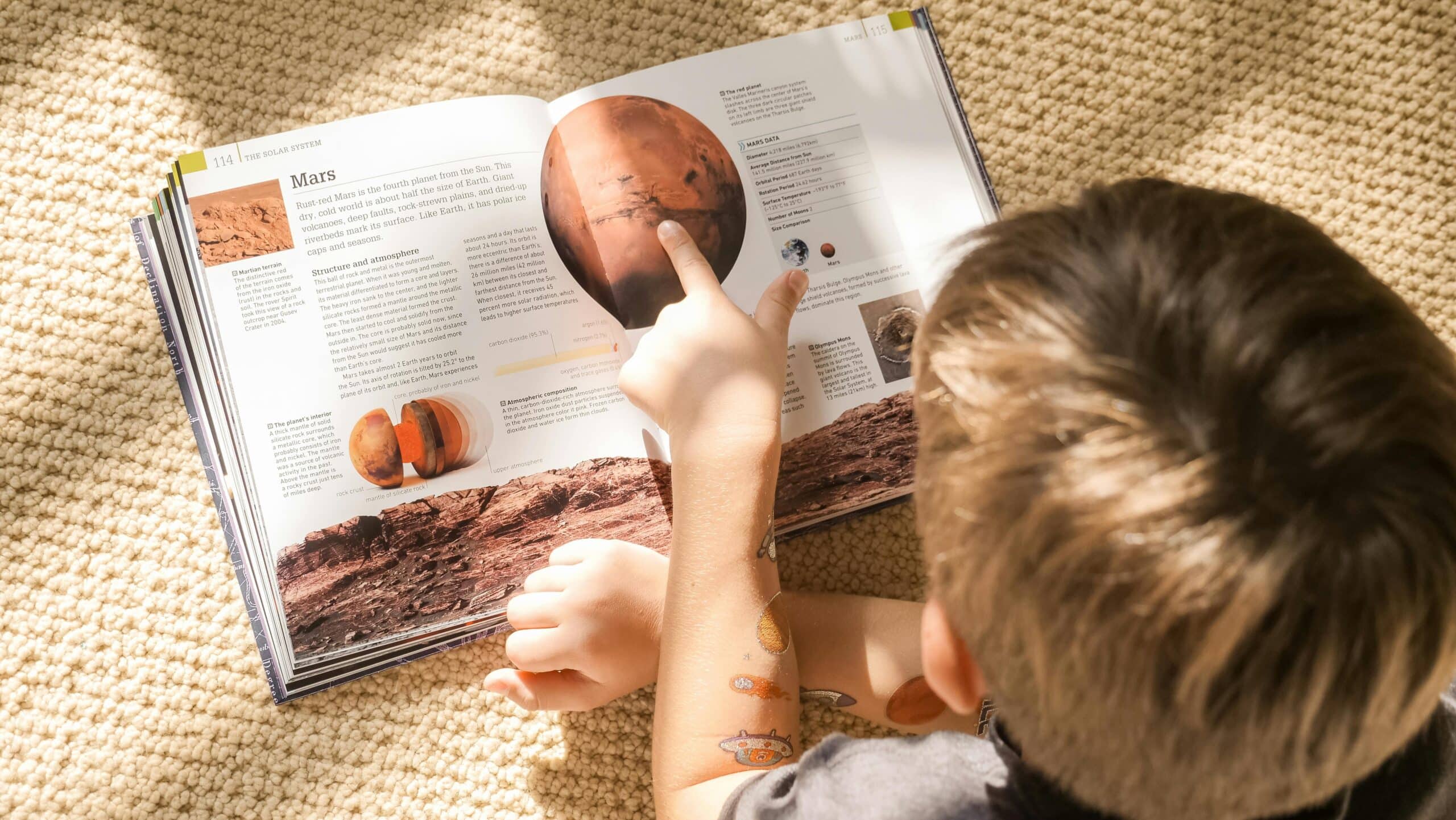 A young boy points at the planet Mars in a book.