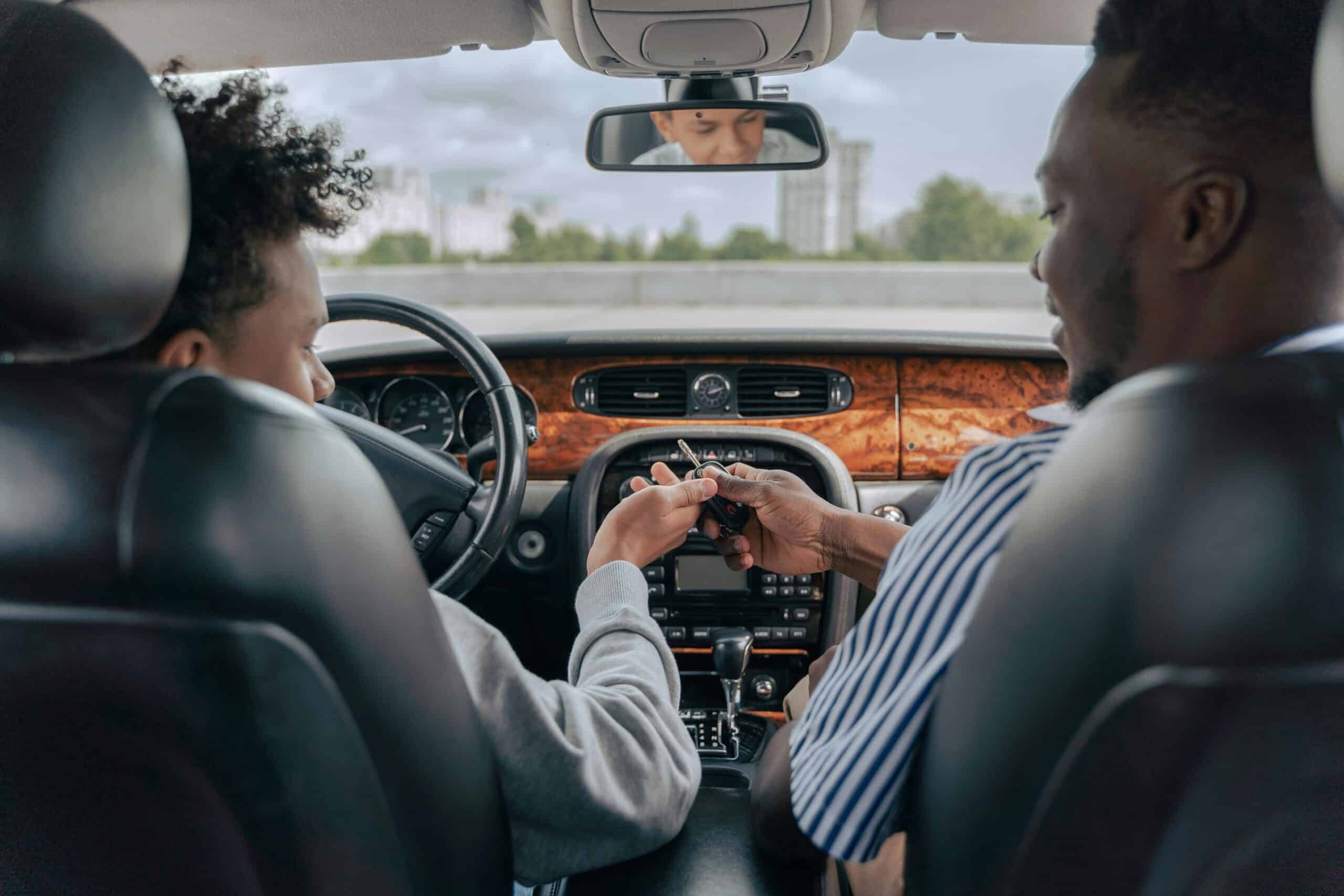 A father exchanges the keys to the car whilst sat in the front of the car.